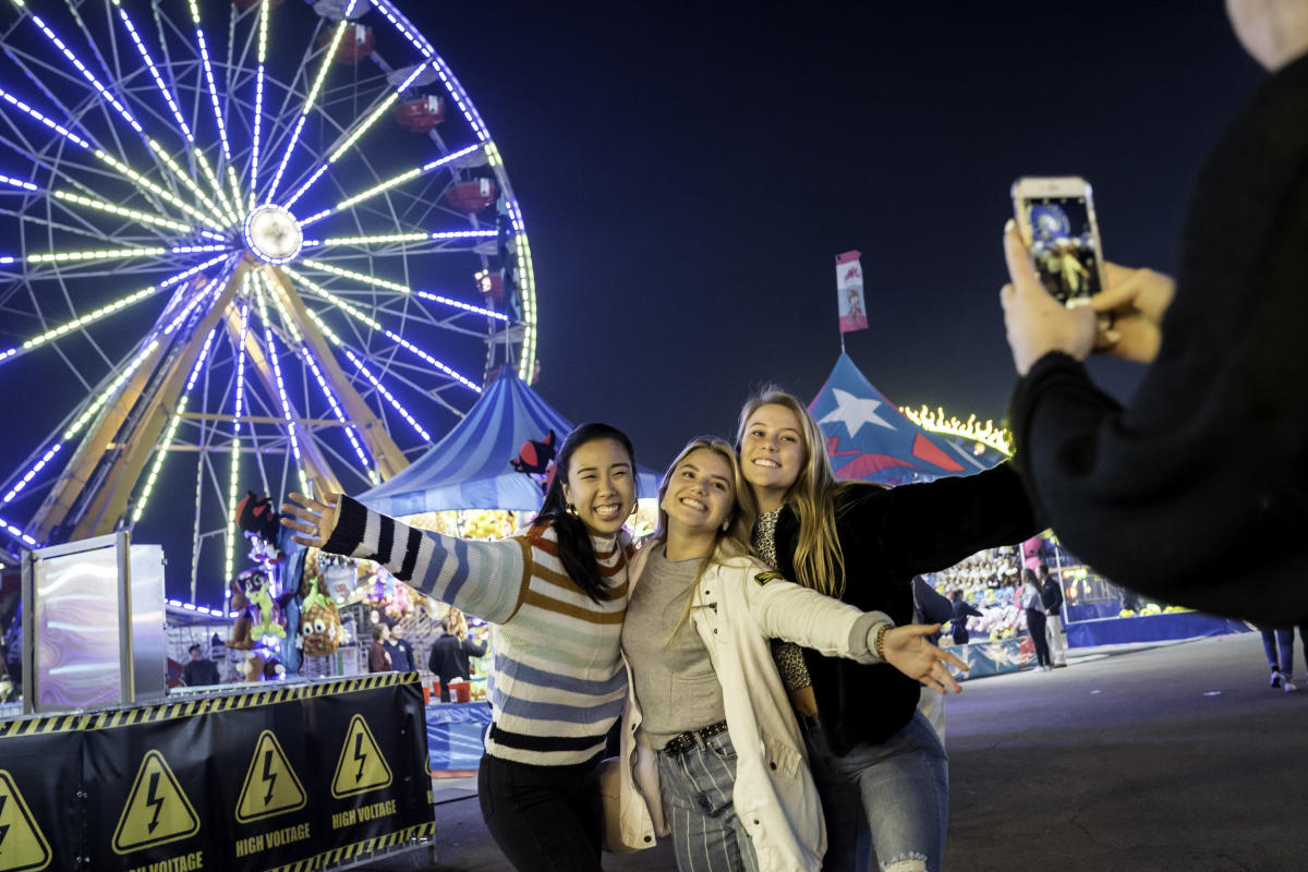 Group of girls posing for photo in front of Ferris wheel lights at State Fair