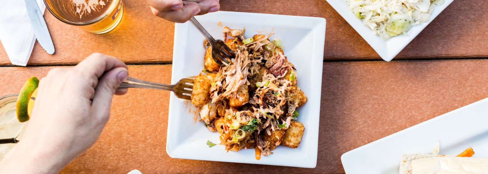 Two hands using forks to grab food off a plate in the center